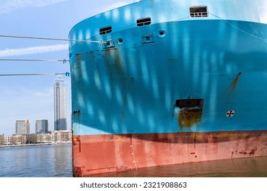 Close up view of the red and blue colored bow a ship with anchor hole, Load line mark and with patchy paintwork with in background the Maas river in Rotterdam, the Netherlands