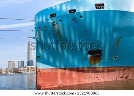 Close up view of the red and blue colored bow a ship with anchor hole, Load line mark and with patchy paintwork with in background the Maas river in Rotterdam, the Netherlands