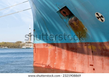 Close up view of the red and blue colored bow a ship with anchor hole, Load line mark and with patchy paintwork with in background the Maas river in Rotterdam, the Netherlands