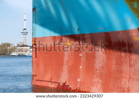 Close up view of the red and blue colored bow a ship with anchor hole, Load line mark and with patchy paintwork with in background the Maas river in Rotterdam, the Netherlands