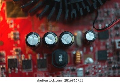 Close up view of red electronic circuit board with capacitors and cooling elements, showing modern technology, precision engineering and digital hardware details.