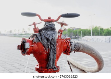 Close view of a red hydrant with attached hose on tiled ground, water dripping and spreading across wet pavement.