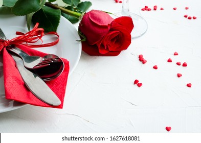 Close up view of restaurant table with romantic place setting with red roses, plates, cutlery on white background. Valentine's Day or romantic dinner concept. Valentine day or proposal background.