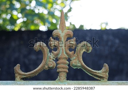Close up view of rusted painted metal finial on top of gate with blurred background. Copy space