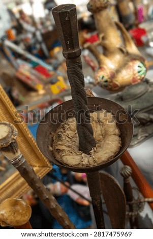 A close view of a rusty hilt and guard of an antique fencing foil displayed with vintage walking sticks at a market. Various items surround the fencing foil.