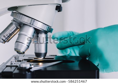 Close up view of scientist hands with gloves set the sample in the microscope for research