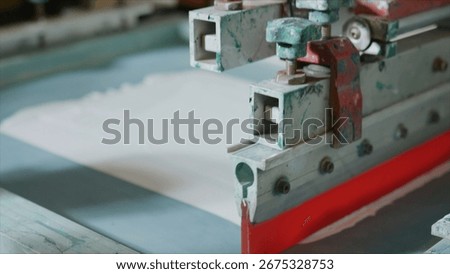 Close up view of a screen printing machine applying white ink onto fabric, highlighting the intricate process of textile printing within a bustling workshop environment