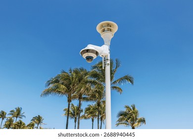 Close up view of security surveillance camera on Ocean Drive with palm trees and clear blue sky on background. Miami Beach. USA.