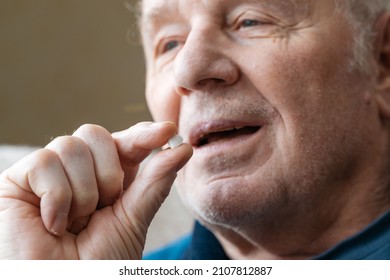 Close Up View Of Senior Male Hand Holding Pill And Taking It. Wrinkled Hand And Face Of Retire Man. Supplements, Longevity Concept