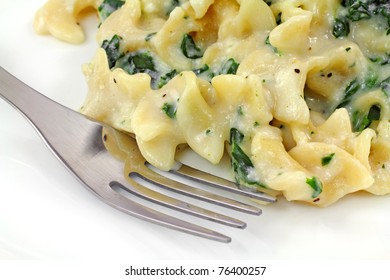 Close view of a serving of ricotta spinach pasta with fork on a white plate.