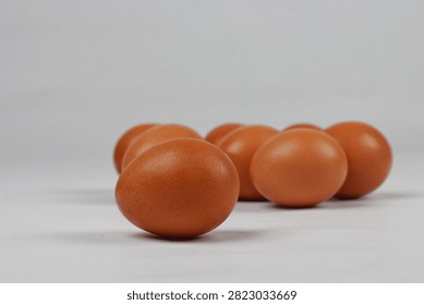 A close up view of several raw brown chicken eggs placed on a clean white surface with soft lighting