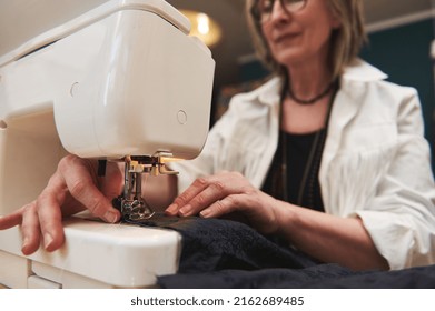 Close Up View Of Sewing Process. Female Hands Stitching Black Fabric On Professional Sewing Machine At Workplace. Seamstress Hands Holding Textile For Dress Production