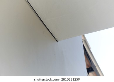 A close up view of a sharp corner on a modern white building facade with a single black wire running along the edge.