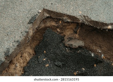 Close up view of sharp cut asphalt edge overhang above eroded soil cavity and collapsed road patch. Concept of pavement failure and construction defect.