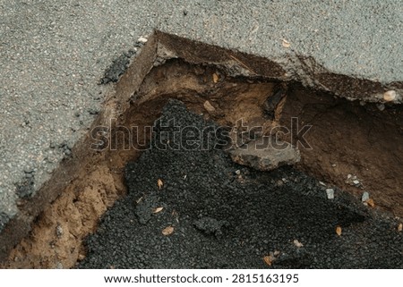 Close up view of sharp cut asphalt edge overhang above eroded soil cavity and collapsed road patch. Concept of pavement failure and construction defect.