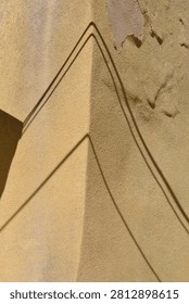 Close up view of sharp diagonal wire shadows forming a geometric pattern on a weathered yellow plaster wall with peeling paint