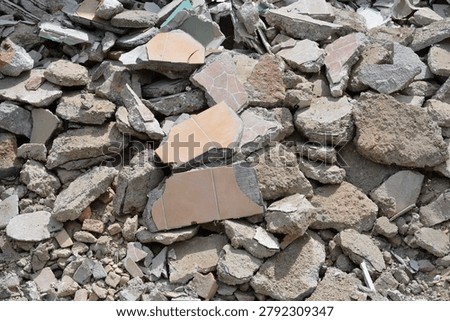 A close up view of shattered ceramic floor tiles mixed with concrete debris at a house renovation site.