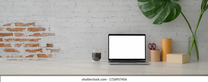 Close Up View Of Shipping Company Office Desk With Mock-up Laptop, Coffee Cup, Supplies, Boxes, Decoration And Copy Space On Marble Desk  