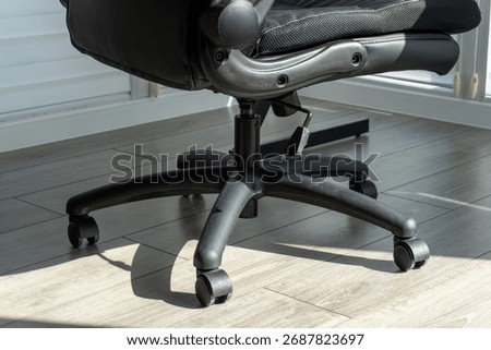 A close up view showcasing the lower section of a contemporary black adjustable office chair. The robust five-star base with smoothly rolling casters sits on a pale wood grain laminate floor. 