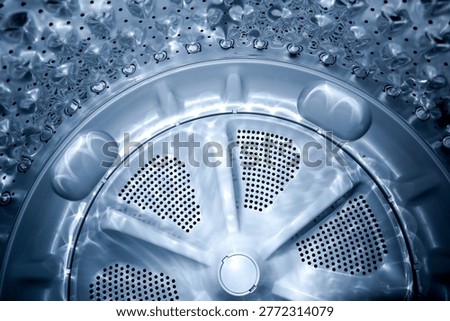 Close up view of a silver washing machine pulsator plate and stainless steel drum with water drainage holes and light reflections