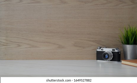 Close up view of simple workplace with  copy space, camera, notebook and tree pot on white desk with modern rustic wall