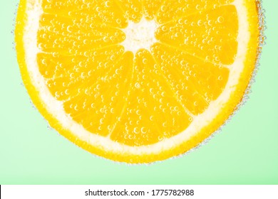 Close Up View Of A Slice Of Orange In Soda Water With Bubbles. Summer Drink Concept.