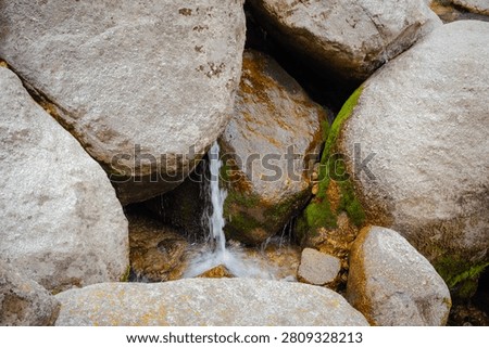 A close up view of a small mountain stream trickling through large textured rocks covered in green moss at Kareri Lake.