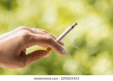 Close up view of smoker holding a cigarette in hand with nature background. Woman with tobacco in her hand surrounded by a natural environment. Cigarette consumed between the fingers. tobacco concept