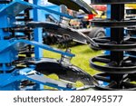 A close view of smooth disc blades mounted on an agricultural disc harrow shows multiple metal discs arranged in a staggered row on a blue frame. The assembly is designed for soil preparation, breaking clods, and mixing crop residue during field cultivation.