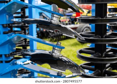 A close view of smooth disc blades mounted on an agricultural disc harrow shows multiple metal discs arranged in a staggered row on a blue frame. The assembly is designed for soil preparation, breaking clods, and mixing crop residue during field cultivation.