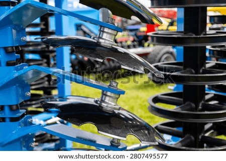 A close view of smooth disc blades mounted on an agricultural disc harrow shows multiple metal discs arranged in a staggered row on a blue frame. The assembly is designed for soil preparation, breaking clods, and mixing crop residue during field cultivation.