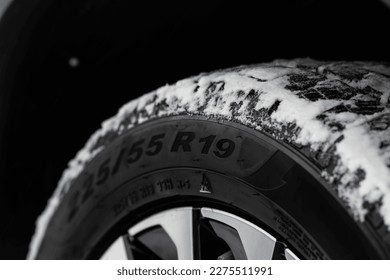 Close up view of snowy tire with tire width, height and wheel diameter designation. Winter tire size types labels.