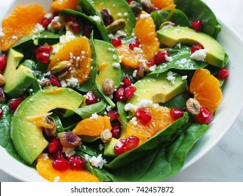 close up view of spinach, avocado salad with orange, pomegranate and pistachio in white bowl on marble background 