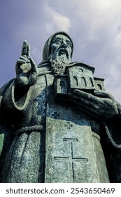 A close up view of the statue of Saint Methodius holding a church in Skopje Macedonia during daylight with a cloudy sky