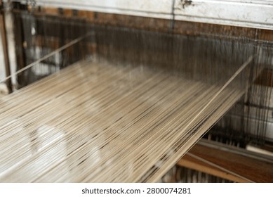 Close up view of stretched warp threads on a traditional wooden handloom. Indonesian authentic tenun fabric production workshop.