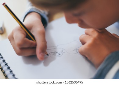 Close Up View Of Student Drawing With Pencil. Boy Doing Homework Writing On A Paper. Kid Hold A Pencil And Draw A Manga At Home. Teen Drawing Sitting At The Table. Education Art Talent Ability Concept