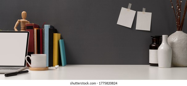 Close up view of study table with copy space, mock up laptop, books, supplies and ceramic vases on white table 