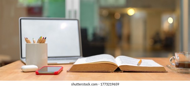 Close up view of study table with opened book, mock up laptop, smartphone, stationery and coffee cup on wooden table - Powered by Shutterstock