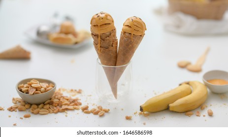 Close Up View Of Summer Dessert With Peanut Butter Banana Flavour Ice-cream Cones, Topping And Copy Space On White Desk Background