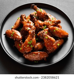 Close up view of sweet and spicy chicken wings on plate over dark stone background. 