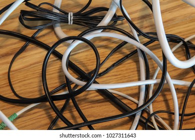 Close up view of tangled black and white wires and cables plugged in the router and socket on the wooden floor of the apartment, chaos of the household