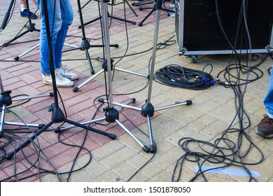 Close Up View Of Tangled Black Wires And Cables Plugged And Microphone Stand On The Ground, Chaos After Open-air Concert