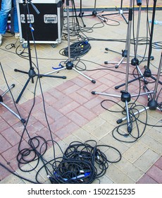 Close Up View Of Tangled Black Wires And Cables Plugged And Microphone Stand On The Ground, Chaos After Open-air Concert