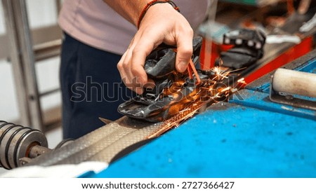 Close up view of technician hands sharpening ski edges on a grinding machine. Flying sparks highlight precise manual work, professional ski service and preparation of winter sports equipment for the season.
