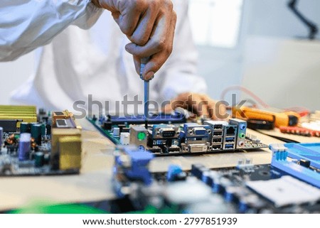 Close view of a technician using a screwdriver on a computer motherboard at a workbench with electronic parts and tools, showing hardware repair, assembly and technology service.