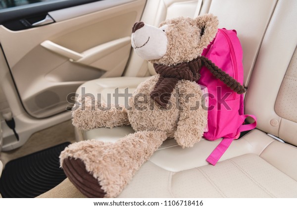 close up view of teddy bear with pink backpack on\
seat in car
