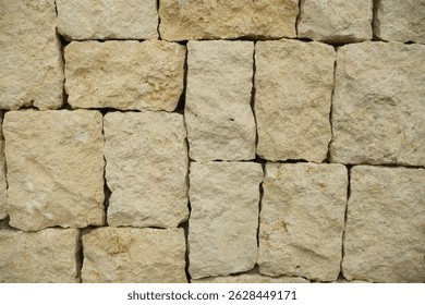 A close up view of a textured rectangular limestone block stone wall