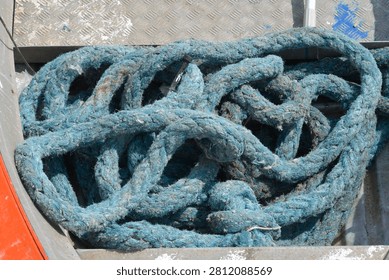 Close up view of a thick tangled blue nautical rope lying on a metal deck inside an old boat hull