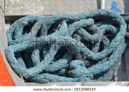 Close up view of a thick tangled blue nautical rope lying on a metal deck inside an old boat hull