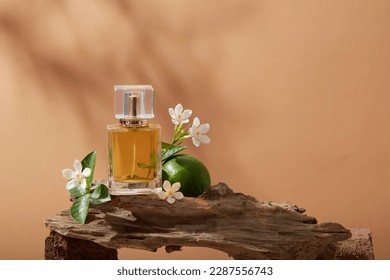 Close up view of a tree branch with Lime, several white flowers and a perfume glass bottle containing yellow liquid of Lime (Citrus aurantiifolia) extract. Empty label for branding mockup